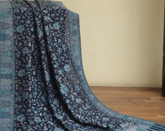 Può includere: Tessuto blu scuro con motivo floreale e bordo turchese. Il tessuto è drappeggiato, rivelando un design dettagliato di fiori e foglie. Il bordo presenta motivi geometrici e a righe.