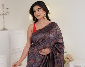 May include: A woman wearing a dark blue and gold paisley patterned saree. The saree has a decorative border with a floral design. The woman is wearing a red sleeveless top.