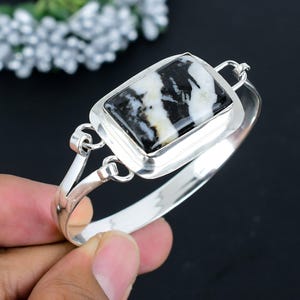 May include: A silver bangle bracelet with a black and white agate stone set in a rectangular frame. The bracelet has a hinged clasp.