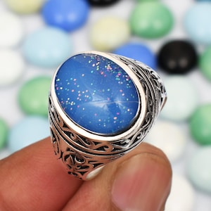 May include: A silver ring with an oval blue stone set in a filigree design. The stone has a glittery finish.