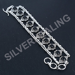 May include: A silver-toned bracelet featuring two parallel chains connected by eight decorative links, each set with a smooth, round, black cabochon stone. The bracelet includes a hook clasp and a short extender chain with three circular links.