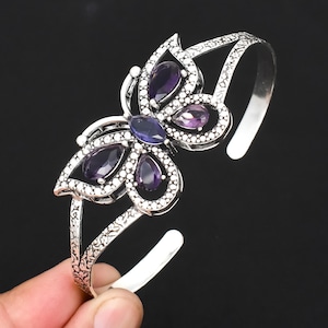 Peut inclure: Un bracelet jonc en argent en forme de papillon avec des pierres précieuses violettes et bleues. Le bracelet est ouvert et présente un design texturé.