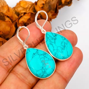May include: A pair of teardrop-shaped earrings featuring bright turquoise stones with dark veining, set in silver-toned metal with lever-back closures. The text SILVERHEALINGS is visible across the image, overlaying the earrings and skin.
