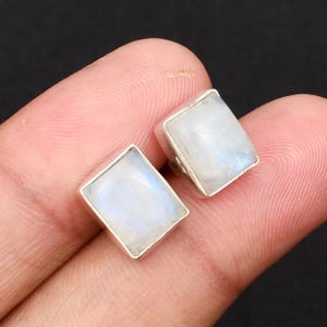 May include: A pair of silver earrings featuring rectangular moonstone gemstones. The stones are a milky white colour with a subtle iridescent sheen.