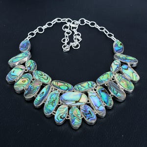 May include: A silver necklace with a large, multi-colored abalone shell pendant. The pendant is made up of several oval-shaped pieces of abalone shell, each with a different iridescent pattern. The necklace is a statement piece that would be perfect for a special occasion.