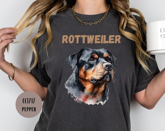 May include: A dark gray t-shirt with a watercolor illustration of a Rottweiler dog's head. The text "ROTTWEILER" is printed in brown above the dog's head.