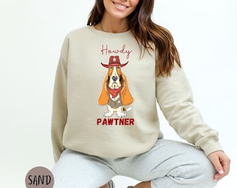 May include: A beige sweatshirt with a cartoon basset hound wearing a cowboy hat and bandana. The text "Howdy Pawtner" is printed below the dog.