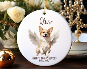 May include: White ceramic ornament with a brown and white corgi dog with angel wings. The ornament has the name "Oliver" and the text "Forever in our hearts 2009-2024".