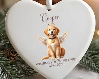 May include: White heart-shaped ornament with a golden retriever angel illustration. The dog has wings, a halo, and a heart-shaped pendant. The ornament has the name "Cooper" and the text "Wishing You Were Here 2012-2024".
