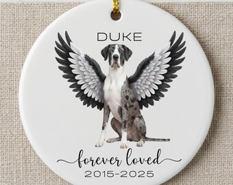 May include: A white ceramic ornament with a Great Dane illustration, wings, and the text "DUKE" at the top. Below the dog is the phrase "forever loved" and the years "2015-2025". The ornament hangs from a gold cord.