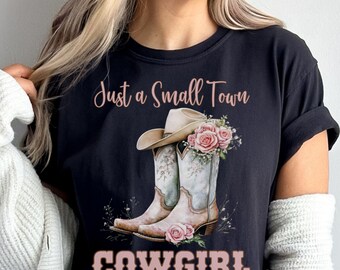 May include: Black t-shirt with a graphic featuring a cowboy hat, boots, and pink roses. The text "Just a Small Town" is above the graphic, and "COWGIRL" is below it in pink letters.