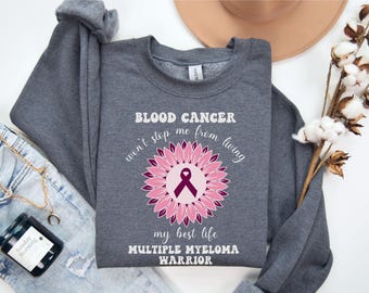 May include: Gray sweatshirt with a pink and purple sunflower design and the text "BLOOD CANCER won't stop me from living my best life MULTIPLE MYELOMA WARRIOR".