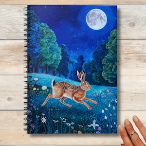 May include: A spiral bound notebook with a blue and green illustration of a hare running through a forest at night under a full moon. The hare is brown and white and the forest is filled with flowers.