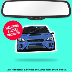 May include: Blue Subaru car air freshener hanging from a rearview mirror. The air freshener has a matching sticker included. "Matching Sticker Included!" is written in red on a white circle.