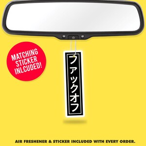 Könnte beinhalten: Ein schwarzer und weißer Auto-Lufterfrischer mit dem japanischen Text "ファックオフ", der an einem Rückspiegel hängt. Ein roter Kreis mit dem Text "MATCHING STICKER INLCUDED!" befindet sich in der linken unteren Ecke des Bildes.
