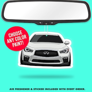 以下が含まれることがあります： 白い車の芳香剤。黒いグリルがあり、赤い円に「CHOOSE ANY COLOR PAINT！」の文字が書かれています。芳香剤は、ターコイズブルーの背景に対して、車のバックミラーから吊り下げられています。