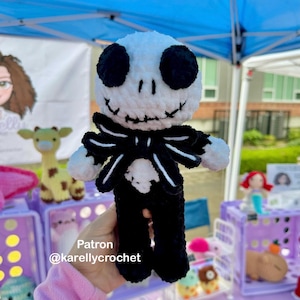 Puede incluir: Muñeco de ganchillo de Jack Skellington, con cabeza blanca, ojos negros y boca cosida. Viste un traje negro con pajarita blanca. El texto "Patron @karellycrochet" es visible. Producto hecho a mano.