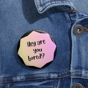 May include: A black and white button with a pink and yellow gradient background. The button says "Hey are you bored?"