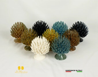 Puede incluir: Surtido de adornos de piña de cerámica en varios colores, incluyendo blanco, negro, marrón, verde y azul. Los adornos están dispuestos en círculo sobre una superficie blanca. Hecho a mano en Italia.