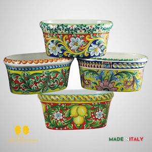 Puede incluir: Cuatro macetas ovaladas de cerámica con diseños florales pintados a mano en tonos de amarillo, verde, rojo y azul. Las macetas están apiladas una encima de la otra. La maceta inferior tiene un diseño de limón. El texto "MADE IN ITALY" es visible en la parte inferior de la imagen.