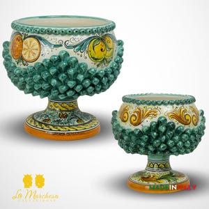 May include: Two ceramic bowls with green pine cone-shaped edges and colorful floral designs. The bowls are on a white background.