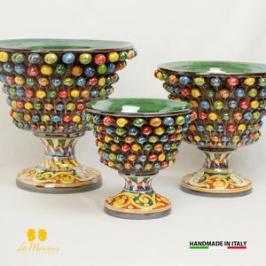 Op de afbeelding: Drie keramische kommen met groene toppen en kleurrijke, ronde accenten. De kommen staan op een witte achtergrond. De kommen zijn allemaal van verschillende grootte en hebben een uniek ontwerp.