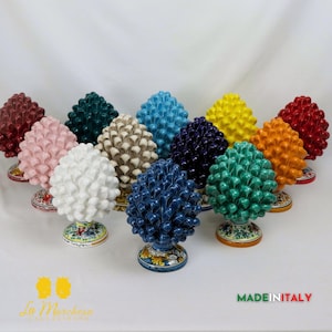 Puede incluir: Una colección de 12 adornos de piña de cerámica en varios colores, incluyendo rojo, rosa, blanco, verde, azul, amarillo y naranja. Los adornos están todos pintados a mano con detalles intrincados y tienen un diseño italiano tradicional.  MADE IN ITALY.