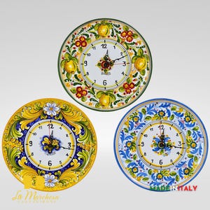 Peut inclure: Trois horloges murales décoratives en céramique avec des motifs floraux et fruités. Les horloges présentent des cadrans blancs avec des chiffres et des aiguilles noirs. Les cadrans sont entourés de bordures jaunes, bleues et vertes avec des motifs floraux et fruités.