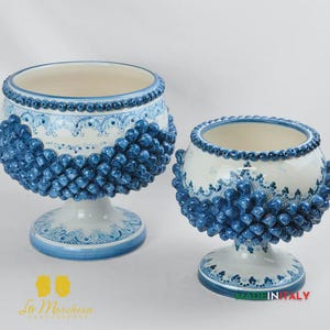 Könnte beinhalten: Zwei dekorative Keramikschalen in Weiß und Blau. Die Schalen haben ein detailliertes Design mit blauen Akzenten und einem strukturierten, erhabenen Muster. Die Schalen stehen auf Sockeln und haben einen detaillierten Rand.