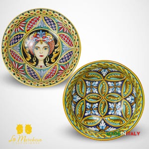 May include: Two ceramic bowls with colorful hand-painted designs. One bowl features a woman's face with intricate details, while the other bowl has a geometric pattern with blue, green, and yellow accents.