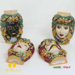 Könnte beinhalten: Vier Keramikkopfskulpturen mit detaillierten Gesichtszügen und aufwendigen Kopfbedeckungen. Zwei stehen aufrecht, zwei liegen. Die Gesichter sind in verschiedenen Hauttönen bemalt, mit leuchtenden Farben und goldenen Akzenten.