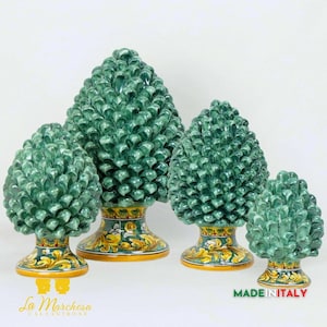 Könnte beinhalten: Vier Keramik-Pinienzapfen-Skulpturen in verschiedenen Größen. Die Pinienzapfen sind grün und haben eine detaillierte, strukturierte Oberfläche. Die Basen der Skulpturen sind mit gelben, grünen und blauen floralen Mustern verziert. Die größte Pinienzapfen-Skulptur ist 30 cm hoch.