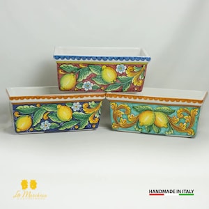 May include: Three rectangular ceramic planters with a lemon motif. The planters are decorated with hand-painted lemons, leaves, and flowers. The planters are in shades of blue, green, and pink.