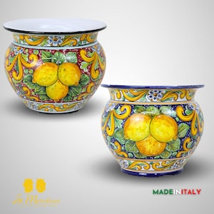 May include: Two ceramic flower pots with a lemon design. The pots are decorated with yellow lemons, green leaves, and blue and white floral patterns. The pot on the left has a red background, while the pot on the right has a blue background. Both pots have a white rim and a black rim around the top.