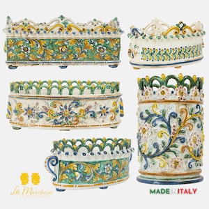 May include: Five ceramic planters featuring intricate floral designs in shades of green, blue, yellow, and white. The planters have a white background with a green rim and are decorated with a variety of floral motifs. The planters are all different shapes and sizes, and they are all made in Italy.