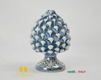 Puede incluir: Escultura de cerámica con forma de piña, con esmalte azul y blanco. La base presenta un diseño decorativo con detalles verdes, azules y blancos. La escultura está etiquetada como "MADE IN ITALY".