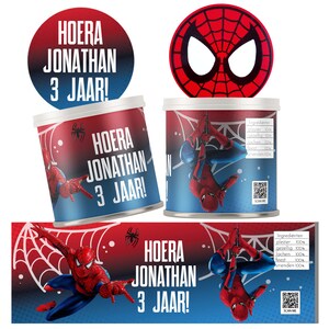 Op de afbeelding: Een set Spiderman-themafeestdecoraties. Het ontwerp heeft een rood-blauwe kleurstelling met de tekst "HOERA JONATHAN 3 JAAR!". De afbeelding bevat een Spiderman-masker, een rond label en cilindrische containers.