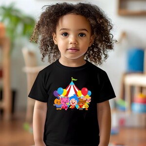 a little girl with curly hair wearing a t - shirt with cartoon characters on it