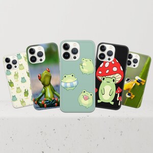May include: Five different phone cases with various frog and mushroom designs. The cases are all white with a clear plastic back and feature different colored frogs and mushrooms.
