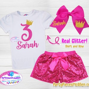 May include: A white t-shirt with a pink number 3 and the name "Sarah" in pink glitter, a matching pink bow, and sequined shorts. The bow and shorts have a pink bow. The text "Real Glitter! Shirt and Bow" is also visible.