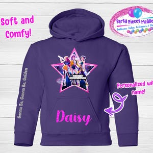May include: A purple hoodie with a star graphic featuring three figures. The name "Daisy" is printed in pink glitter on the front pocket. Text on the sleeve reads "Gonna Be, Gonna Be, Golden." The hoodie is advertised as "Soft and Comfy!" and "Personalized with name!"