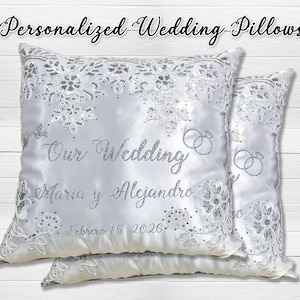 May include: White satin wedding pillows with silver sequin and lace detailing. The pillows are embroidered with the words "Our Wedding", names, and the date "February 15 2026". The image also includes the text "Personalized Wedding Pillows".