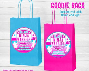 Puede incluir: Dos bolsas de regalo coloridas, una azul y otra rosa, con asas blancas. Cada bolsa presenta una etiqueta circular con el texto "Ellie's Ninja Warrior 8th Birthday" y "Thank You For Coming!". Las bolsas son para una fiesta de cumpleaños.