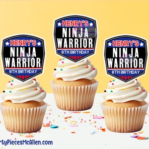 Puede incluir: Tres cupcakes blancos con glaseado blanco y chispas de colores. Cada cupcake tiene una cubierta redonda, negra y azul con estrellas blancas y el texto "HENRY'S NINJA WARRIOR 8TH BIRTHDAY".