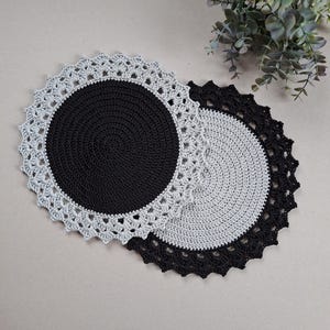 Könnte beinhalten: Zwei gehäkelte Tischsets, eines schwarz mit einem grauen Rand und eines grau mit einem schwarzen Rand. Beide haben eine zarte gehäkelte Kante.