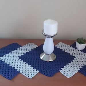 Puede incluir: Un camino de mesa de ganchillo azul y blanco con un candelero blanco y una pequeña planta en maceta sobre una mesa de madera.