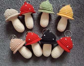 May include: Nine crocheted mushroom keychains in various colors, including red, green, yellow, black, and brown. Each mushroom has white dots on the cap and a white stem.