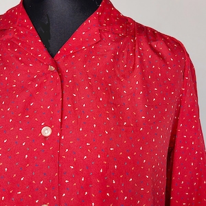 Può includere: Una camicia rossa a maniche lunghe con bottoni e una piccola stampa astratta colorata.