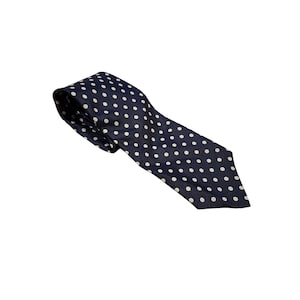 Pode incluir: Uma gravata azul marinho com bolinhas brancas. A gravata é feita de um tecido liso e é adequada para trajes formais ou de negócios. A gravata está em ângulo sobre um fundo branco.