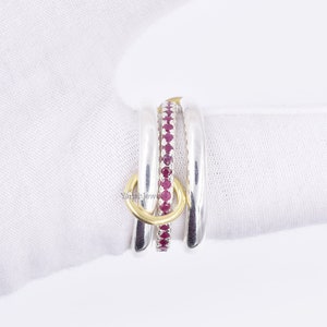 May include: Three silver rings with a gold band and red gemstones. The rings are stacked on top of each other.